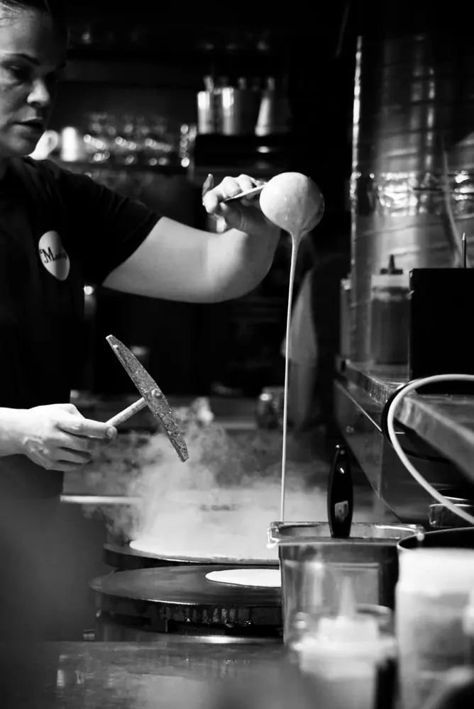 Der Crêpe-Bäcker verstreicht den Teig mit dem Holzrechen auf dem Billig von Mamilig